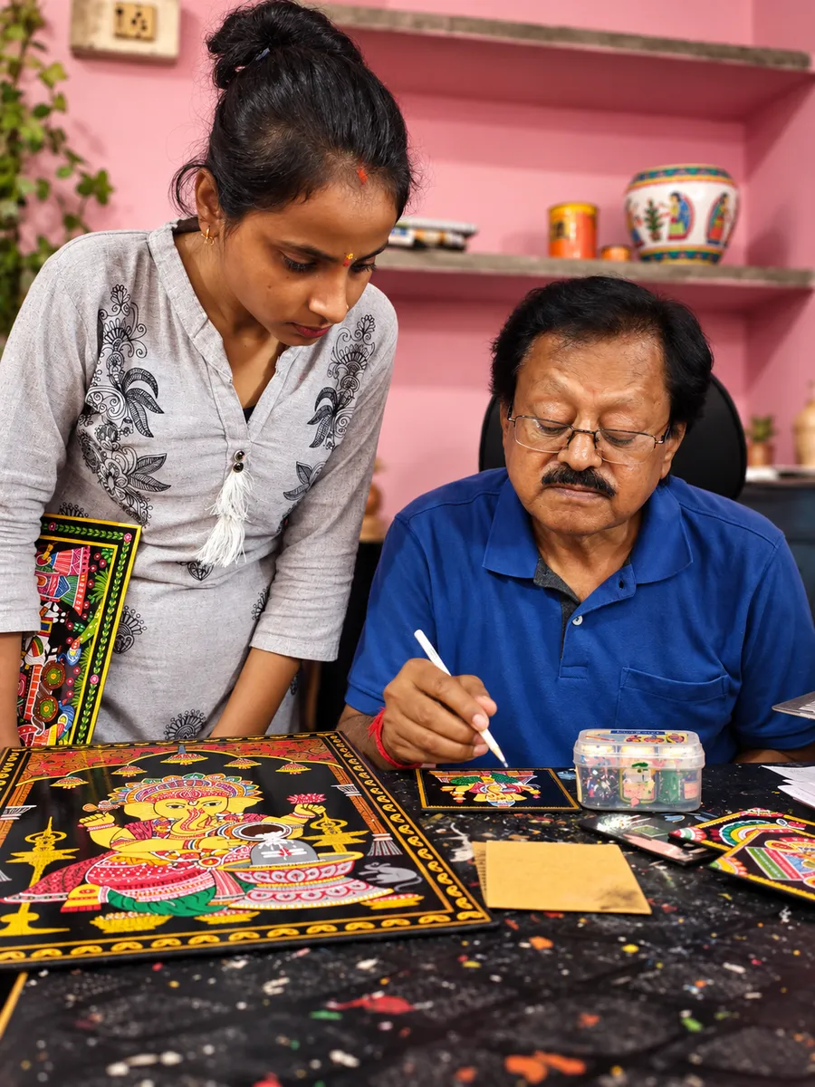 An older artist paints a detailed panel at a table while a younger woman watches closely.