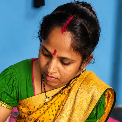 An artist in a green and gold sari paints a blue peacock.