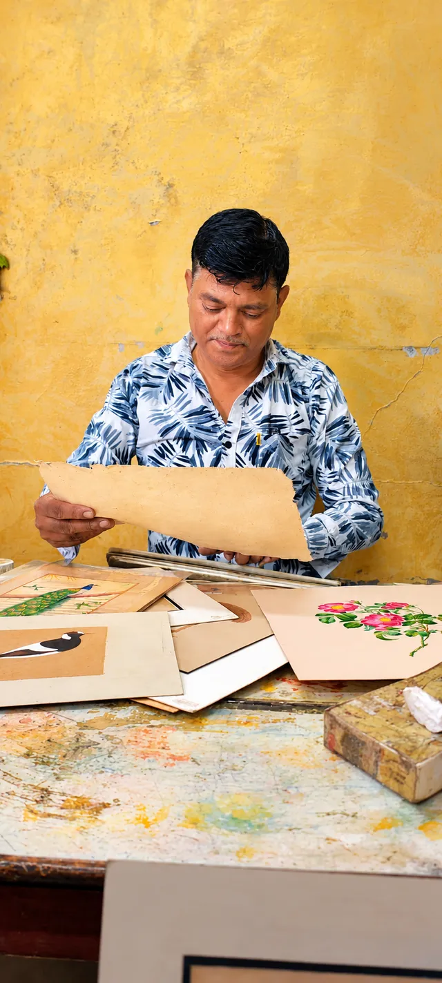Pappu Chand looks over his miniature paintings spread on a table.