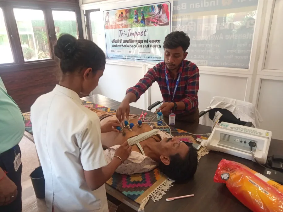 A health worker examines a worker lying on a table at a health camp.
