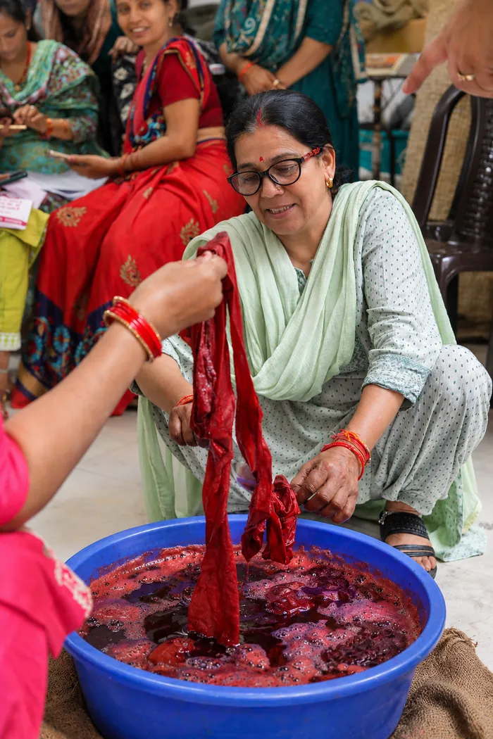 Women lift a length of cloth from a vat of red natural dye during a workshop.